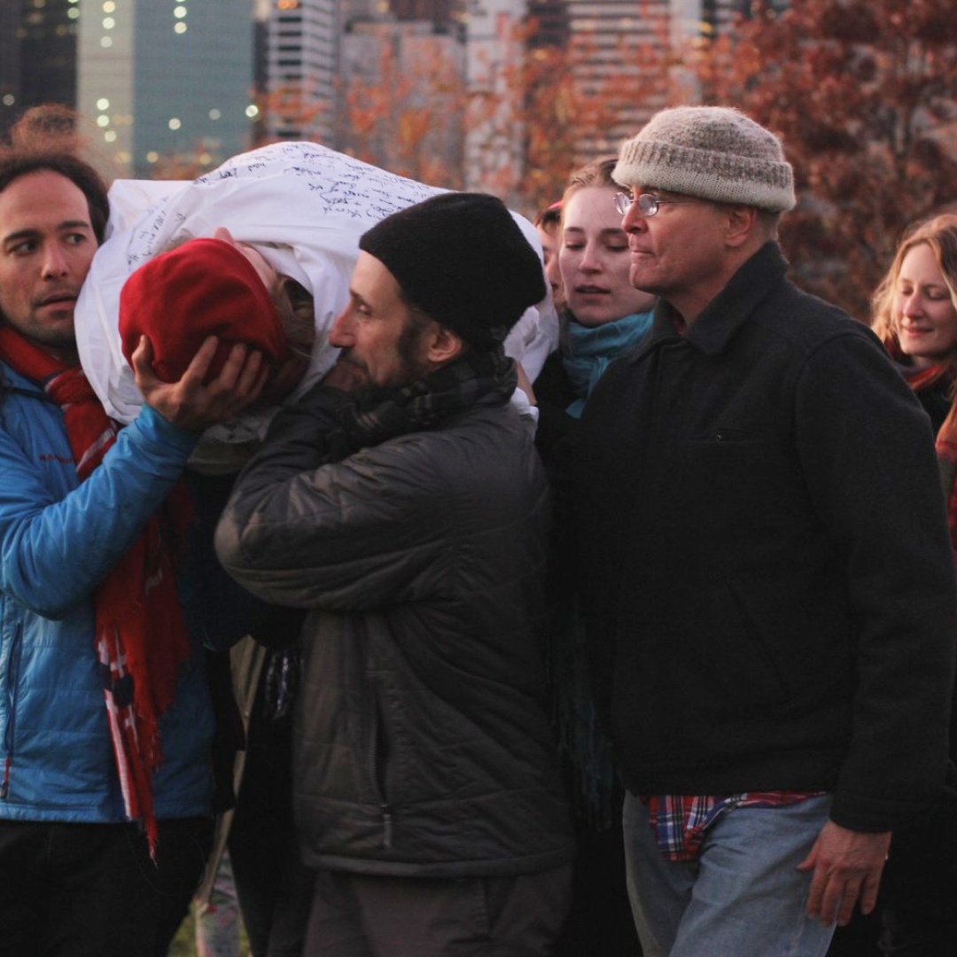 A group gathered closely together outdoors, one person passing a red object to another.