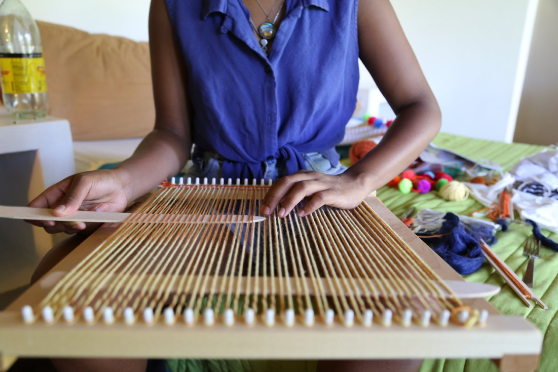 A person threading a warp onto a small hand loom.